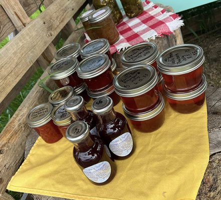 Jars of Frani's homemade jelly and bottles of chokecherry syrup on a yellow cloth at the farmstand
